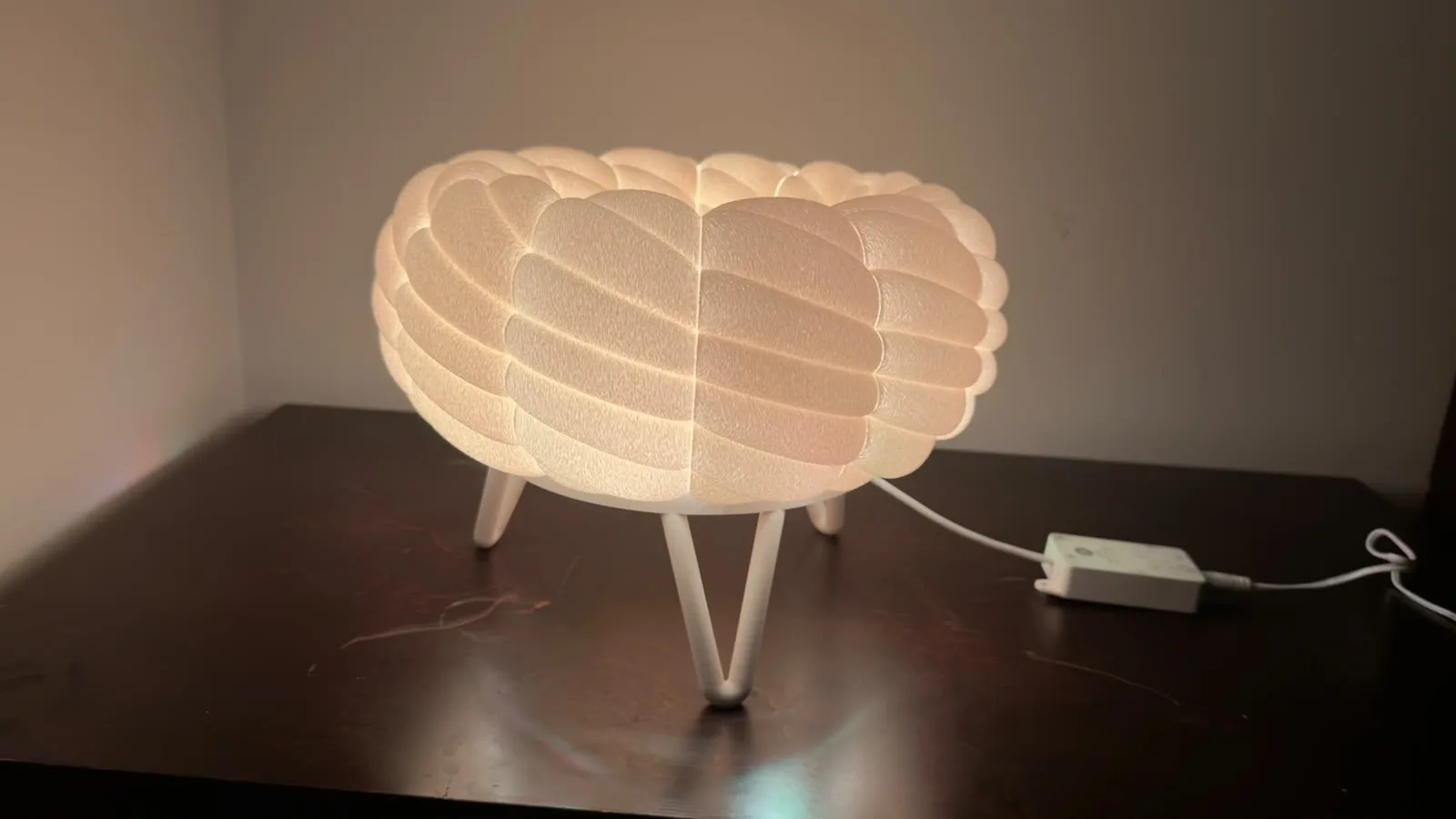 Cloud table lamp on a dark nightstand with its plug-in power adapter beside it