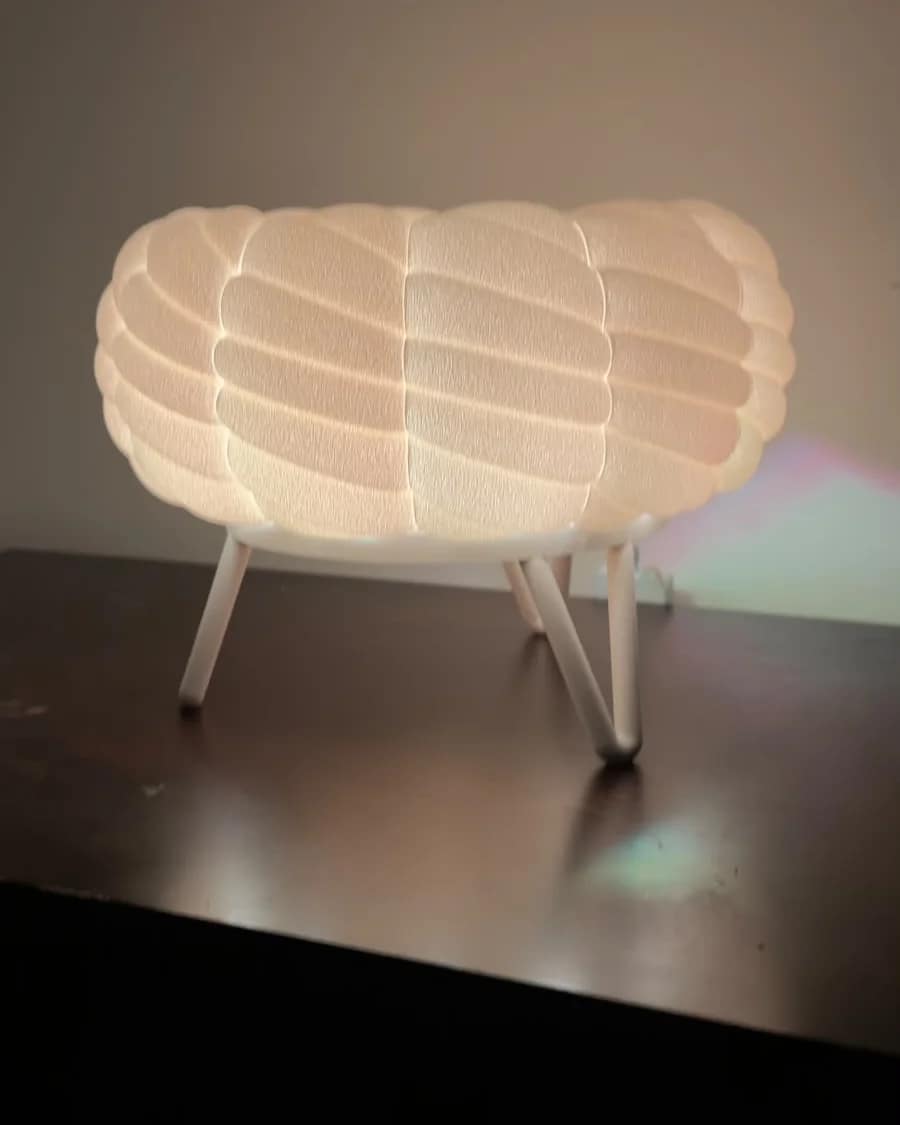 Puffy white 3D-printed cloud table lamp with a textured, knit-like shade on three hairpin legs, glowing warm, made at Shaped For You
