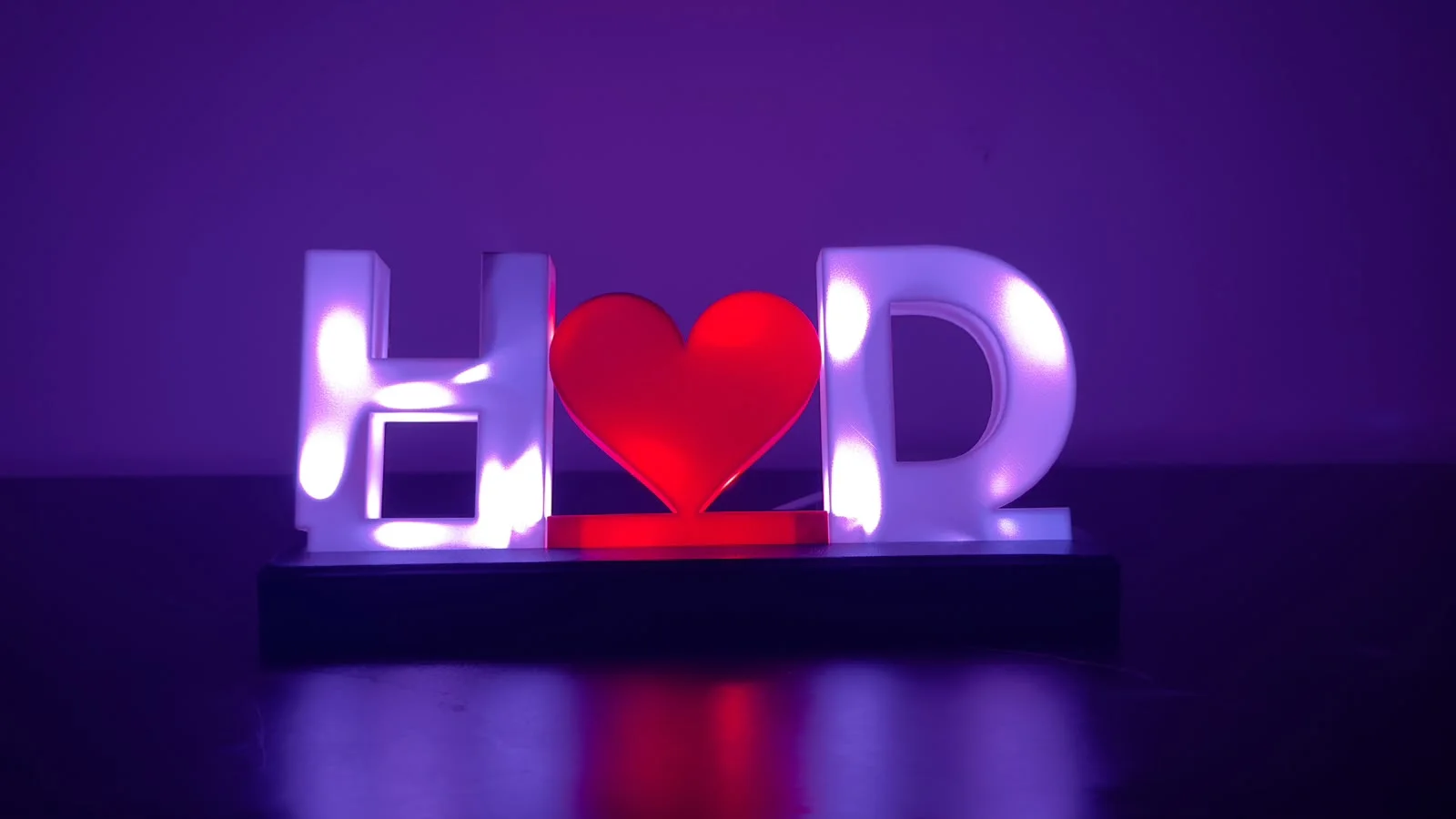 Initials name lamp reading H, heart, D: white letters glowing purple and a red heart, on a dark base