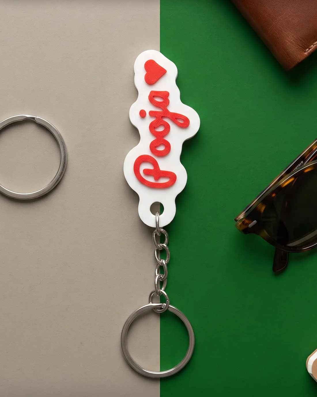 White 3D-printed name keychain reading Pooja in red script with a small red heart, on a silver chain and key ring
